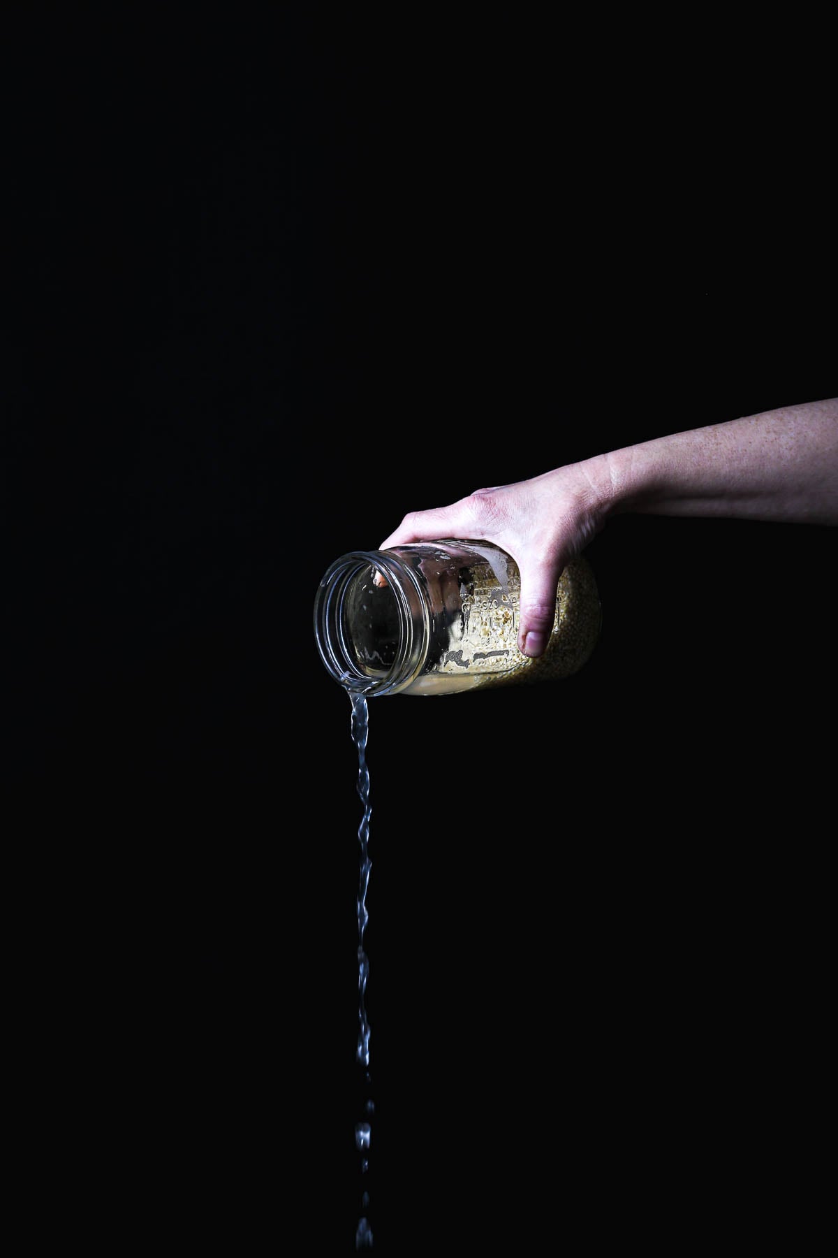 Draining soaked quinoa in a jar after the initial soak before sprouting.