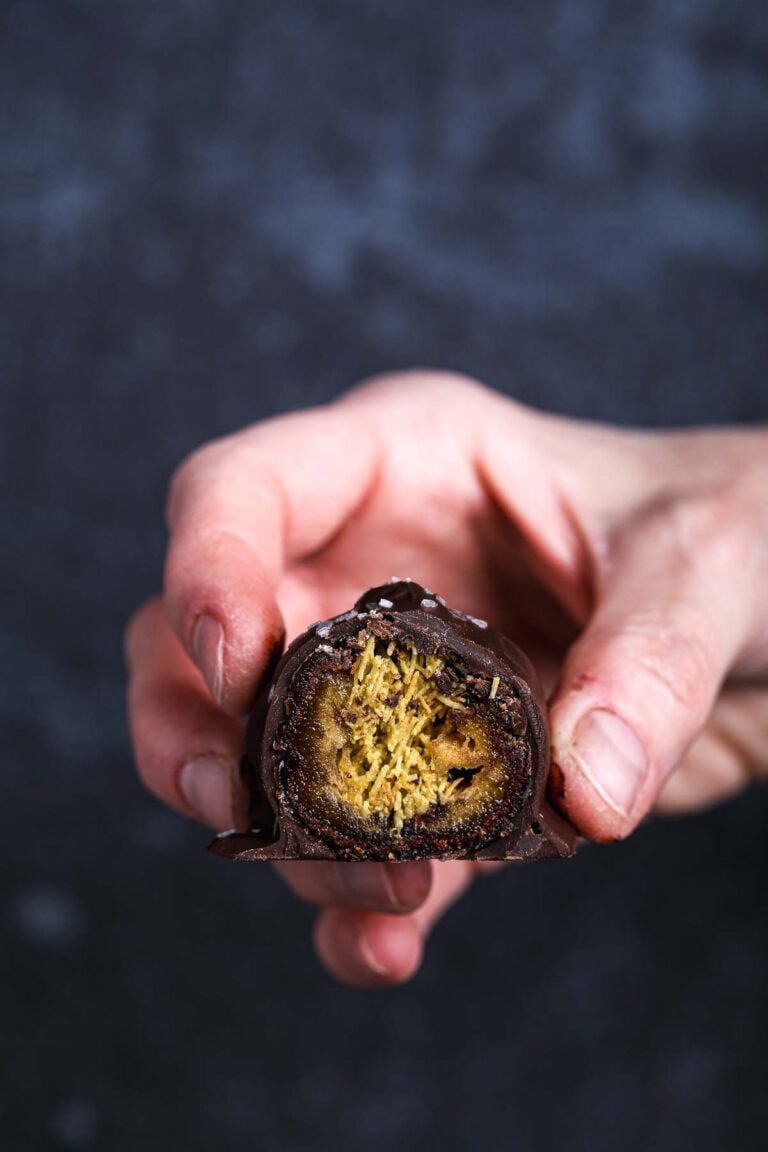 Close-up of a halved Dubai chocolate date showing a soft Medjool date filled with toasted kataifi and pistachio cream, coated in dark chocolate.