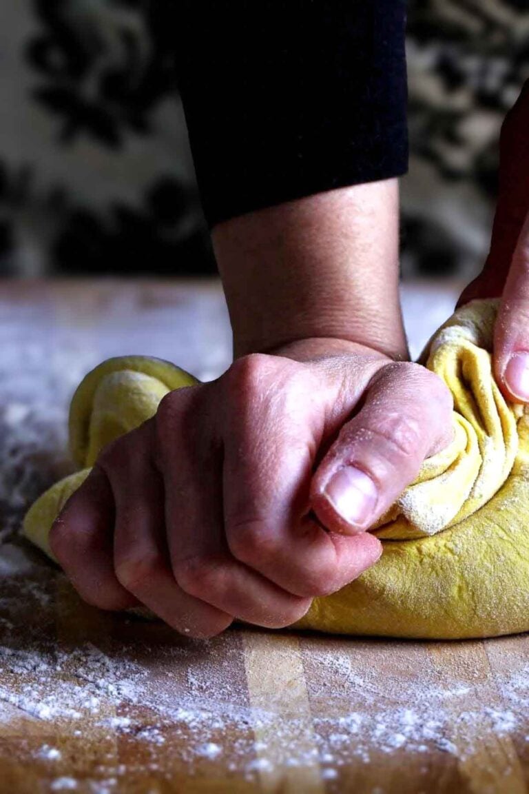 Hand kneading vegan ravioli dough made with silken tofu and semolina on a floured work surface.