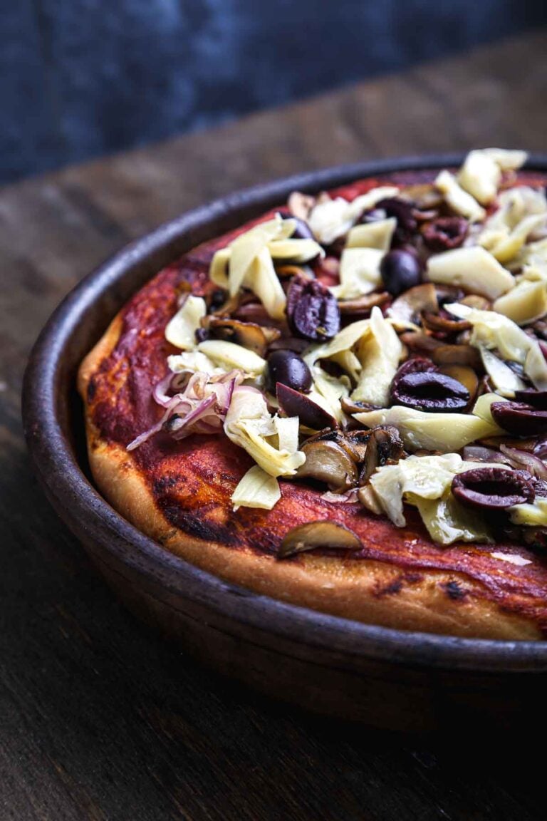 Skillet pizza baked in a round pan and topped with mushrooms, olives, and artichokes.