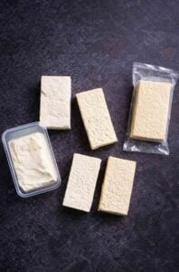 Different types of tofu arranged on a dark surface, from silken to super-firm, showing texture differences.
